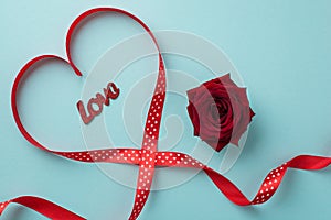 Top view photo of saint valentine`s day decorations red rose inscription love and red silk ribbon heart on isolated pastel blue