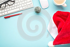 Top view photo of santa claus hat keyboard computer mouse red pen glasses pine toy and cup of hot drinking on isolated pastel blue