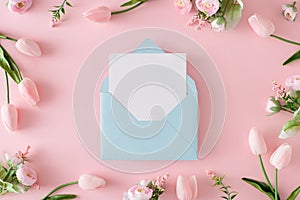 Top view photo of spring flowers and tulips on pastel pink background and open envelope with white card