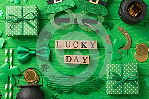 Top view photo of st patricks day decor wooden cubes labeled lucky day party glasses straws green bow-tie gift boxes horseshoe