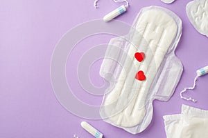 Top view photo of tampons and sanitary napkin with red hearts on isolated pastel lilac background with copyspace