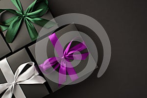 Top view photo of three stylish black gift boxes with purple green and white satin ribbon bows on isolated black background with