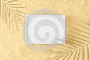 Top view photo of tropical leaf shadows on sandy background and white frame