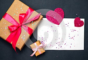 Top view photo of a Valentine`s day decor gift box, paper heart, confetti ,a sheet of paper on a dark gray background
