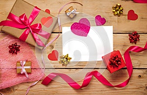 Top view photo of Valentine`s day decor gift box, paper heart, a sheet of paper on a wooden background