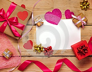 Top view photo of Valentine`s day decor gift box, paper heart, a sheet of paper on a wooden background