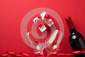 Top view photo of valentine`s day decorations giftbox with bow red curly ribbon small hearts in two wineglasses and wine bottle o