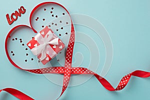 Top view photo of valentine`s day decorations giftbox in red wrapping paper with pattern of hearts confetti red ribbon heart and