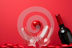 Top view photo of valentine`s day decorations red curly ribbon small heart between two wineglasses and wine bottle on isolated re