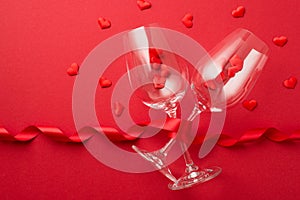 Top view photo of valentine`s day decorations red curly ribbon and small hearts flying out of two wineglasses on isolated red