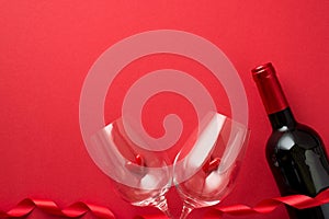 Top view photo of valentine`s day decorations red curly ribbon small hearts in two wineglasses and wine bottle on isolated red