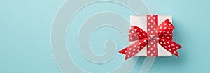 Top view photo of valentine`s day decorations white gift box with red ribbon bow heart pattern on isolated pastel blue background