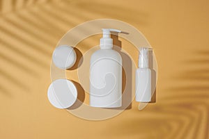Top view photo of white cosmetic bottle, cream jars, spray bottle and tropical leaves shadow