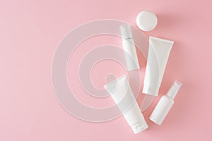 Top view photo of white cosmetic bottles, cream jars and pump bottles without label on pastel pink background