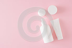 Top view photo of white cosmetic bottles without label and cream jars on pastel pink background