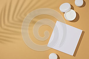 Top view photo of white cosmetic podium, cream jars and tropical leaves shadow on sandy background