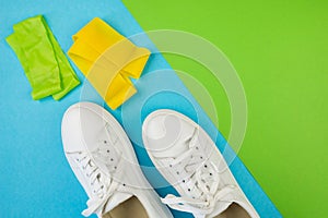 Top view photo of white sneakers, green and yellow fitness rubber bands on blue green background