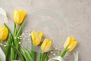 Top view photo of woman`s day composition bouquet of yellow tulips white gypsophila and white ribbon on isolated textured grey