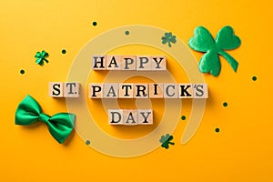 Top view photo of wooden cubes labeled happy st patricks day shamrock shaped confetti and green bow-tie on isolated yellow