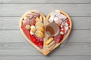 Top view photo of wooden heart shaped serving tray with confectionery candies cookies and glass cup of hot chocolate