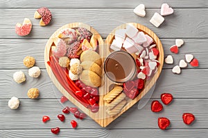 Top view photo of wooden heart shaped serving tray with confectionery candies cookies and glass cup of hot chocolate