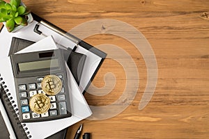 Top view photo of workplace with chancellery black folder organizers calculator pen plant and two gold coins with bitcoin symbol