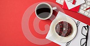 Top view photo of workplace keyboard red binder clip pencil notepads glasses cup of coffee and plate with glazed chocolate