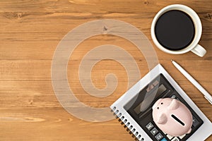 Top view photo of workplace with white cup of coffee piggy bank and calculator on notebook pen on isolated wooden table background
