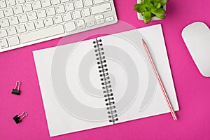 Top view photo of workplace with white keyboard mouse binders plant pencil on open notebook on isolated pink background with