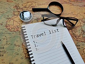 Top view phrase travel list with compass, eye glasses and magnifier on world map.