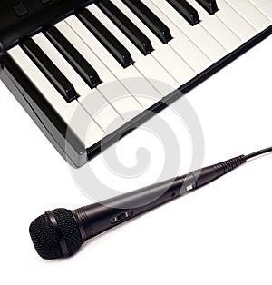 Top view of piano keyboard and black vocal microphone on white background closeup