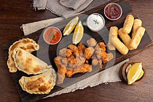 Top view of a picada board with nuggets and tequenos with lemon slices and white and spicy sauces