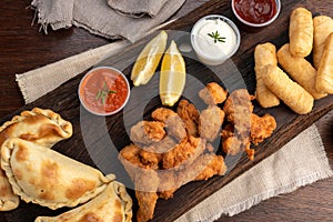 Top view of a picada board with nuggets and tequenos with lemon slices and white and spicy sauces photo