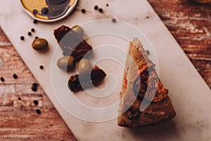 Top view of a pie with tomato slices as a topping placed next to olives and dates on a white surface