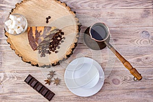 Top view of a piece of chocolate cake on wooden stump with a coffee cup, tea spoon, fork, anise, coffee beans, chocolate bar and b