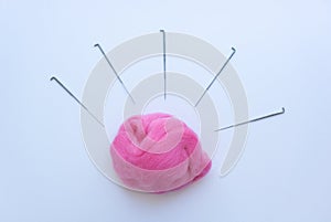 Top view of piece of pink wool surrounded by steel needles on white background. Concept of felting creative hobby. Selective focus
