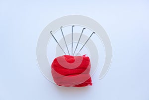 Top view of piece of red wool surrounded by steel needles on white background. Concept of felting creative hobby. Selective focus