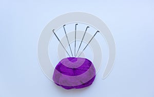 Top view of piece of violet wool surrounded by steel needles on white background. Concept of felting creative hobby. Selective foc