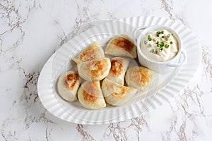 Top view pierogies on a white platter with sour cream and spring onions