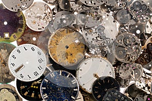 Top view of pile of dials and clockworks from vintage clocks. Faces of white, black and metal old clocks and silver