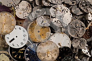 Top view of pile of dials and clockworks from vintage clocks. Faces of white, black and metal old clocks and silver