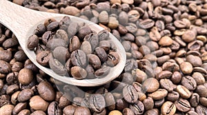 Top view of a pile of scattered aromatic roasted brown coffee beans with a wooden scoop. Coffee beans in a wooden spoon