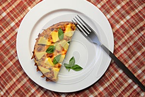 top view of pineapple pizza slice on a white plate, with a fork and knife