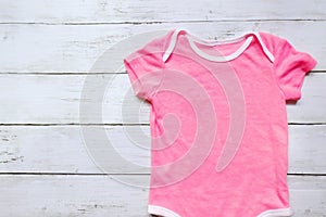 Top view of pink baby romper on white wooden background. Copy space for text or graphic