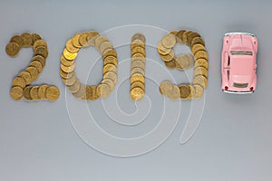 Top view of a pink car figurine next to 2019 written with coins, on gray background