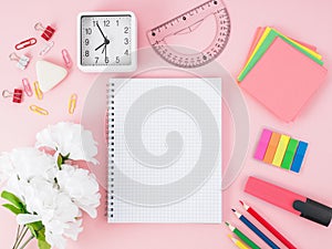 Top view of pink office desktop with notebook in cage, flowers,