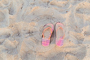 Top view of pink and orange ornamental flip flops at sand on sea beach