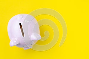 Top view of pink piggy bank on yellow background with copy space