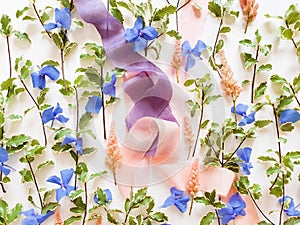 Top view of pink and purple silk ribbons, fresh greens, blue and pink flowers on a white background. Lifestyle, mockup