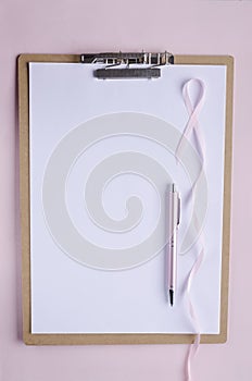Clipboard, white blank paper, pink pen and pink ribbon as a symbol of breast cancer.Pink background, empty space for text photo
